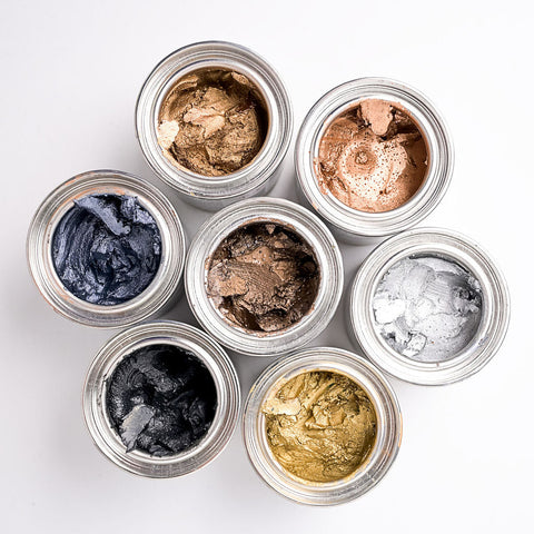 Assorted metallic waxes in small round containers on a white background