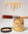 Jar of Dixie Belle Glaze Gold Shimmer with a brush and gold glaze dripping from it on a light gray background.