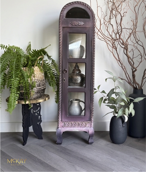 Decorative tall cabinet with ornate design, surrounded by plants and vases on a wooden floor.