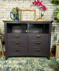 Dark black dresser with gold handles against a brick wall with 'Lost & Found Mercantile' text.