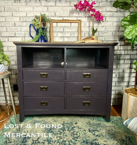 Dark black dresser with gold handles against a brick wall with 'Lost & Found Mercantile' text.