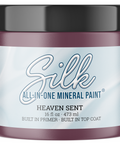 A jar of Silk All-In-One Mineral Paint in the color Heaven Sent, featuring a dark plum-purple container, a black lid, and a light blue and white label.