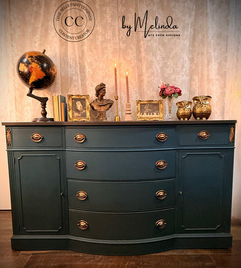 Decorative dresser with various items against a textured wall, featuring the 'CC by Melinda' brand.
