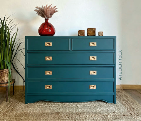 Teal dresser with gold handles against a white wall, featuring a red vase and decorative items.