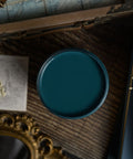 Teal paint container on a wooden surface with dried flowers and an ornate mirror.
