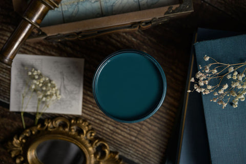 Teal paint container on a wooden surface with dried flowers and an ornate mirror.