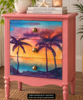 A pink three-drawer nightstand with a colorful tropical sunset palm tree decoupage on the front, shown in a styled room setting with plants and books on top. Label reads "Digital Rendering for Inspiration. Scale and sizing are approximate."