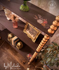 Decorative shelf with various items including a gold frame and a green vase, with 'by Melinda' branding.