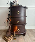 Wooden side table with three drawers, candles, and decorative items on a wooden floor.