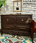 Dark wooden dresser with gold handles in a room with a brick wall and patterned rug.