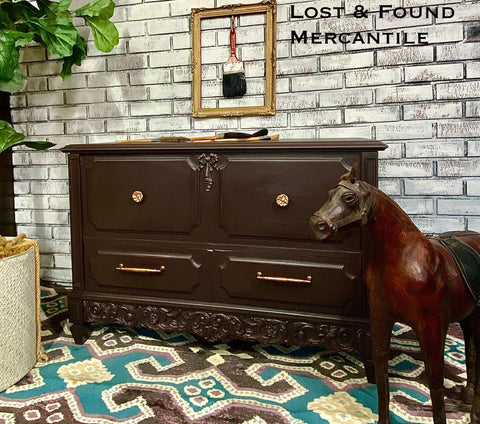 Dark wooden dresser with gold handles in a room with a brick wall and patterned rug.