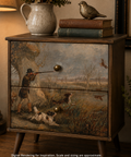 A rustic wooden nightstand with two drawers, featuring a detailed hunting scene painted on the front. The nightstand is styled in a cozy room setting with a lamp, books, a ceramic pitcher, and a bird figurine on top.