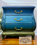 A vintage chest of drawers painted in blue ombre with gold accents and ornate handles, sits on a wooden floor next to white flowers. Label reads “Caribbean, Pacific, Deep Woods, and Gold Digger.”.