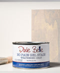 Can of Weathered Gray Dixie Belle gel stain with a brush and stained wood panel on a gray background