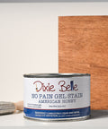 Dixie Belle American Honey No Pain Girl Stain can with a brush and wood sample on a gray background