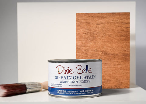 Dixie Belle American Honey No Pain Girl Stain can with a brush and wood sample on a gray background