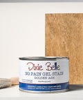 Dixie Belle Golden Ash gel stain can with a brush and sample board on a gray background