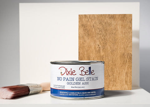 Dixie Belle Golden Ash gel stain can with a brush and sample board on a gray background