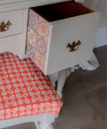 White dresser with a drawer open, revealing a colorful side, on a wooden floor.
