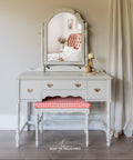 Vintage-style vanity with mirror and chair in a room with curtains and a window.
