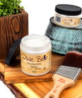 Jars of 'Dixie Belle' glaze on a wooden surface with a brush and plant.