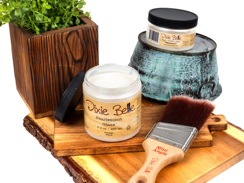 Jars of 'Dixie Belle' glaze on a wooden surface with a brush and plant.