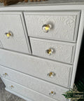 White dresser with decorative embossing and crystal knobs on a neutral background