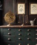 Moody apothecary-style cabinet painted in a deep green finish with vintage brass hardware, styled with antique scientific decor, botanical prints, and dark wood paneling.