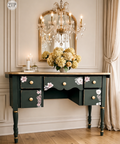 Decorative desk with floral designs in a room with a chandelier and mirror.