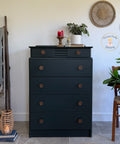 Dark green dresser with decorative items in a room with a ladder, plant, and lantern.