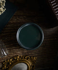 Dark green paint can on a textured surface with decorative items like a miniature Eiffel Tower and mirror.