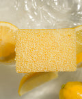 Lemon scrubby soap surrounded by sliced lemons on a reflective surface
