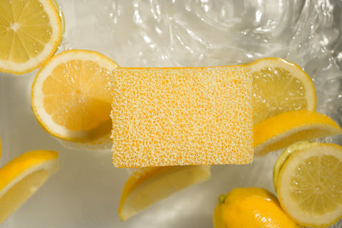 Lemon scrubby soap surrounded by sliced lemons on a reflective surface
