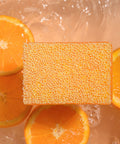 Square orange scrubby soap with sliced oranges on a wet surface