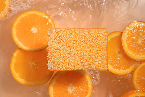 Square orange scrubby soap with sliced oranges on a wet surface