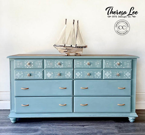 A chalk painted dresser in blue chalk paint, stenciled top drawers, staged with a sailboat on top.