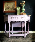 Vintage-style table with decorative items against a dark background, featuring the artist Jodie Flavell Art.
