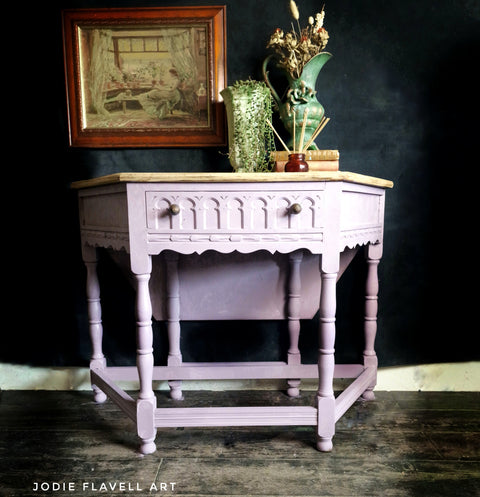 Vintage-style table with decorative items against a dark background, featuring the artist Jodie Flavell Art.