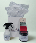 A Dixie Belle gift set featuring a bottle of Pristine Clean Ready to Use, a jar of Silk Paint in Anchor, and a paintbrush, arranged in front of a branded white gift bag with tissue paper.