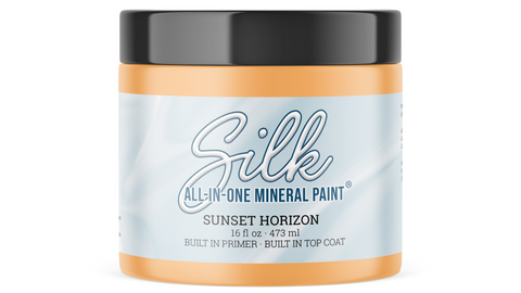 A jar of Silk All-In-One Mineral Paint in the shade Sunset Horizon, featuring an orange paint jar with a black lid and a light blue label.