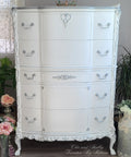 Decorative white dresser with intricate details in a room with plants and flowers.