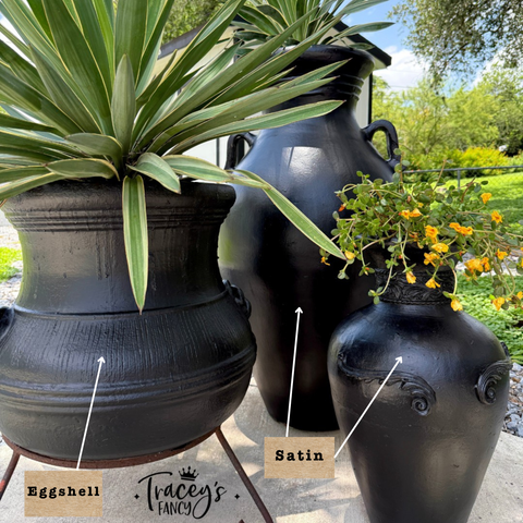 Three black decorative ceramic pots in different shapes, shown outdoors with plants. The pots are labeled 'Eggshell', 'Satin', and the image includes the brand name 'Tracey's Fancy' at the bottom.