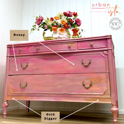 Pink dresser with gold accents in a room with flowers on a table.