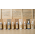 Nine bottles of Dixie Belle VooDoo Stains in varying shades are lined up on a table. The background features wooden planks in different natural tones, complementing the stains.