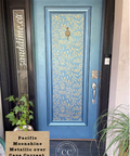 A front door painted in a metallic blue finish with a lighter blue leaf pattern across the center panel. The door has a brass knocker, silver handle, and lockset.