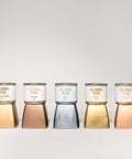 Seven jars of Gilding Wax in different colors—black, antique gold, bronze, zinc, gold, copper, and silver—are lined up on a white background, each shown above a swatch of its corresponding color.