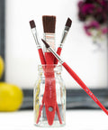 Belles and Whistles Artist Brushes. Artist brushes in mason jar set against an unfocused backdrop consisting of apples, a picture frame and purple and orange flowers.
