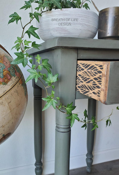 Belles and Whistles Botanical - Silkscreen Stencil provides an extra decorative touch to any project!
The side of a console table with the drawer open, on the side of these drawers is the Botanical - Silkscreen Stencil. Staged with a white bowl, greenery and a cut off Globe.