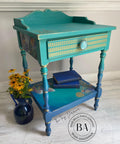 Belles and Whistles Botanical - Silkscreen Stencil provides an extra decorative touch to any project!
End table with a green blended to blue paint along with Botanical - Silkscreen Stencil with gold on the front of the drawer. Staged with a blue flower vase and yellow flowers to the side of the table.