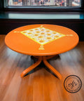 Orange painted table makeover. Crazy Daisy stencil applied on the table top in white, yellow, and orange with a yellow border. Yellow tassels painted on each corner of the border.
